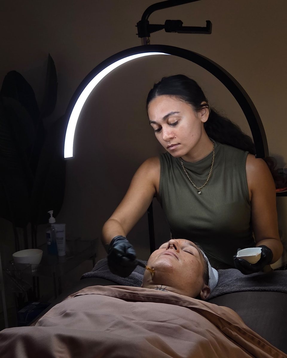 Samantha giving a facial in her treatment room under a soft ring light